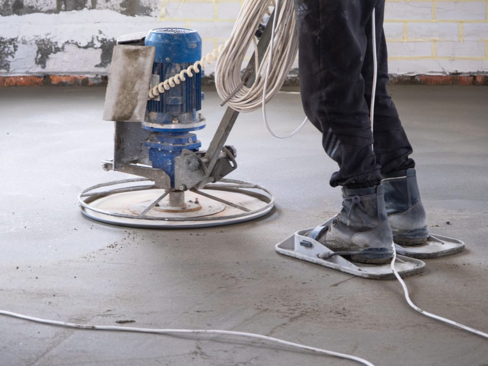 Ramming and grinding of semi-dry floor screed by a machine with a rotating disk for leveling. Construction of a concrete floor in the house, a master with special equipment.